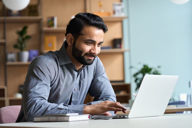 A man sitting at a table in an office works at his laptop.